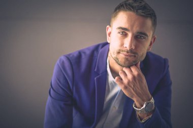 Gri arka planda yalnız oturan genç iş adamı.