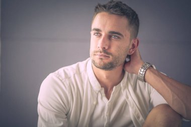 Gri arka planda yalnız oturan genç iş adamı.