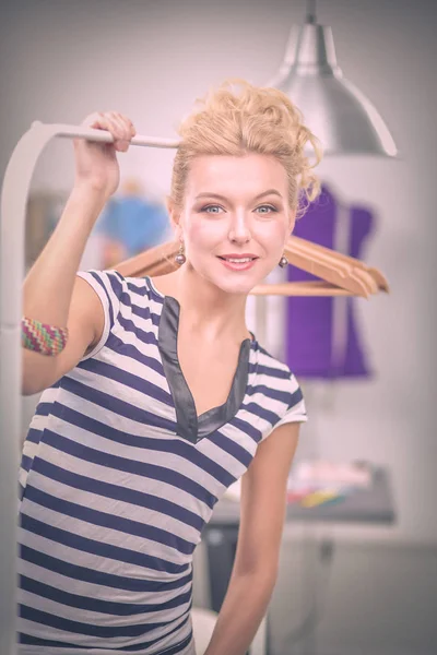 Mooie jonge stylist in de buurt van rack met hangers in office — Stockfoto