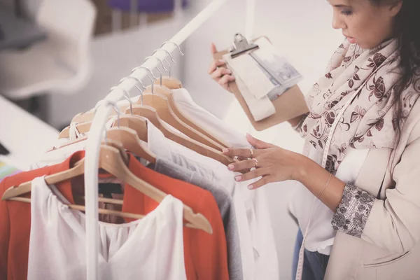 Mooie jonge stylist in de buurt van rack met hangers in office — Stockfoto