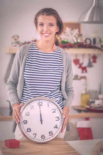 Happy young woman showing clock in christmas decorated kitchen — Stock Photo, Image