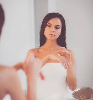 Çekici genç bir kadın yüzüne krem sürüyor.