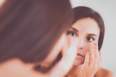 Çekici genç bir kadın yüzüne krem sürüyor.