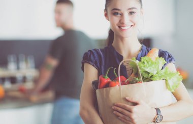 Mutfakta genç bir çift, alışveriş torbası taşıyan bir kadın.
