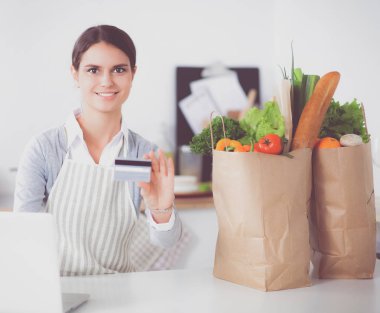 Mutfakta bilgisayar ve kredi kartı kullanan gülümseyen bir kadın.