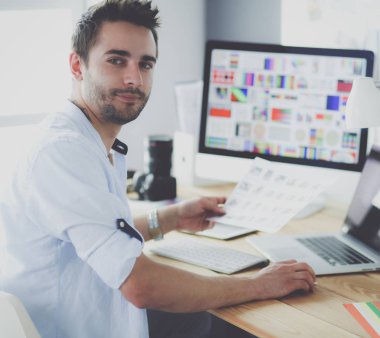 İnternette çalışırken bilgisayarın ve dizüstü bilgisayarın önünde grafik stüdyosunda oturan genç tasarımcının portresi.