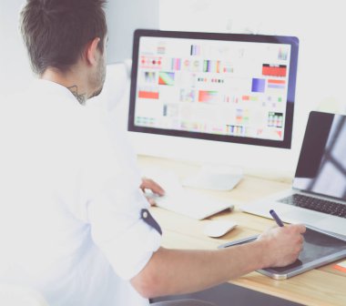 İnternette çalışırken bilgisayarın ve dizüstü bilgisayarın önünde grafik stüdyosunda oturan genç tasarımcının portresi.