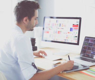 İnternette çalışırken bilgisayarın ve dizüstü bilgisayarın önünde grafik stüdyosunda oturan genç tasarımcının portresi.