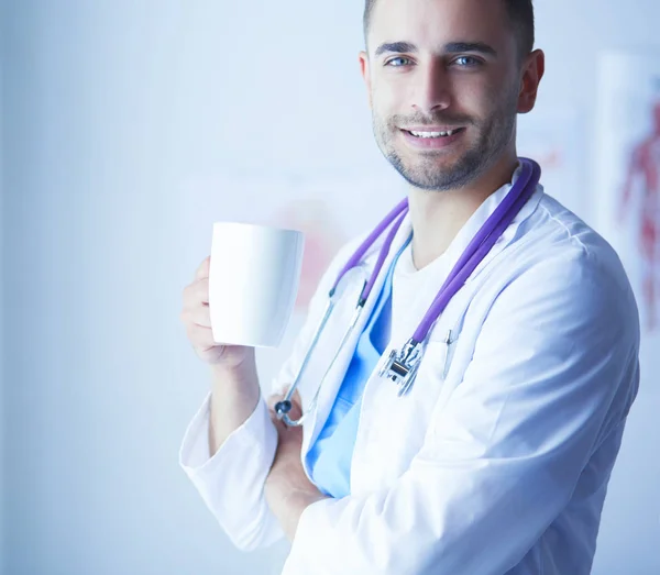 Young doctor with coffee cup in medical office