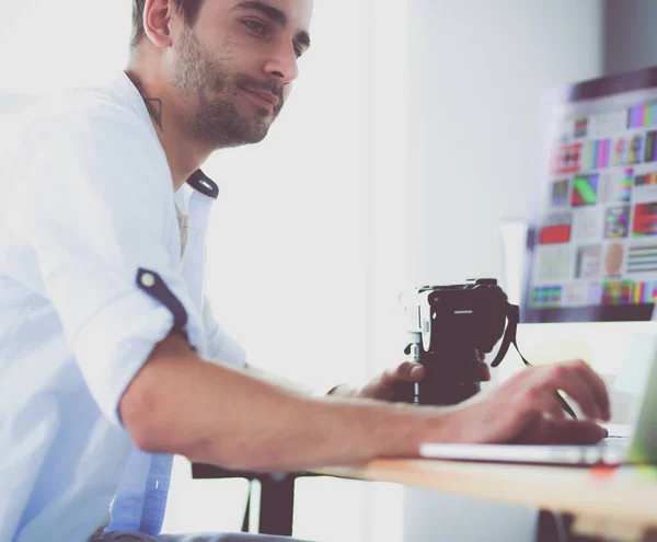 Retrato del joven diseñador sentado en el estudio gráfico frente a la computadora portátil y el ordenador mientras trabaja en línea. — Foto de Stock