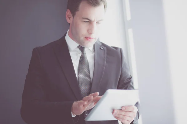 Retrato de jovem empresário no cargo com grande janela. Empresário usando o computador tablet e olhando para a câmera. — Fotografia de Stock