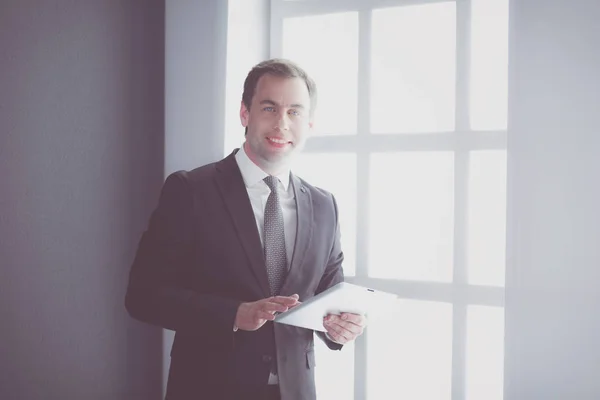 Retrato de un joven hombre de negocios en la oficina con gran ventana. Empresario usando tableta y mirando a la cámara. —  Fotos de Stock
