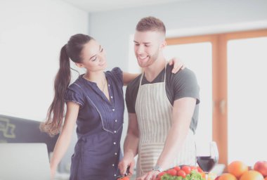 Sebze doğrayan genç bir adam ve mutfakta dizüstü bilgisayarı olan bir kadın.