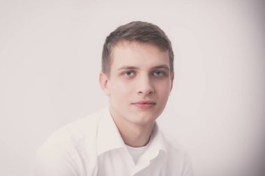 Gri arka plan üzerinde oturan gülümseyen genç adam portresi. Genç adam portresi