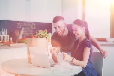 Sebze doğrayan genç bir adam ve mutfakta dizüstü bilgisayarı olan bir kadın.