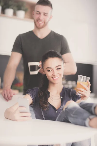 Casal feliz usando smartphone sentado na cozinha — Fotografia de Stock