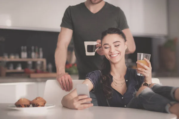 Pareja feliz usando smartphone sentado en la cocina —  Fotos de Stock