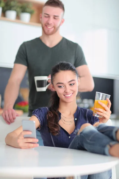 Casal feliz usando smartphone sentado na cozinha — Fotografia de Stock