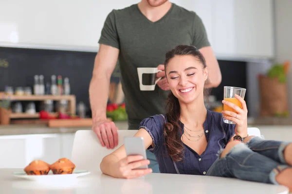 Pareja feliz usando smartphone sentado en la cocina —  Fotos de Stock