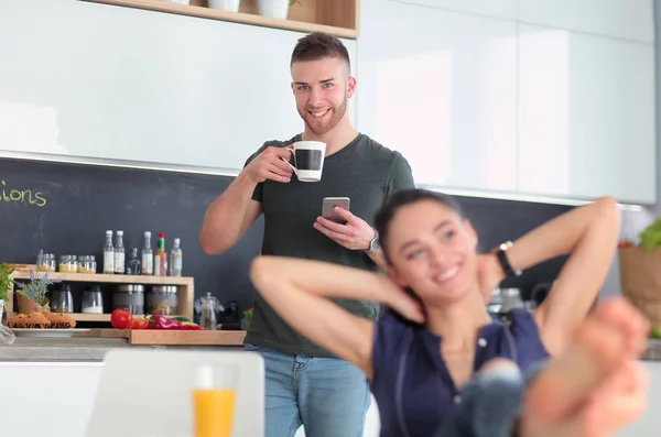 Pareja feliz usando smartphone sentado en la cocina —  Fotos de Stock