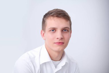Gri arka plan üzerinde oturan gülümseyen genç adam portresi. Genç adam portresi