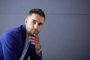 Gri arka planda yalnız oturan genç iş adamı.