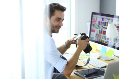İnternette çalışırken bilgisayarın ve dizüstü bilgisayarın önünde grafik stüdyosunda oturan genç tasarımcının portresi.