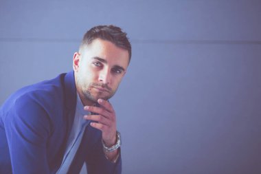 Gri arka planda yalnız oturan genç iş adamı.