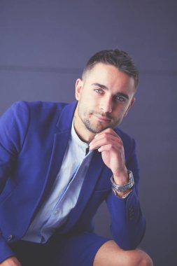 Gri arka planda yalnız oturan genç iş adamı.