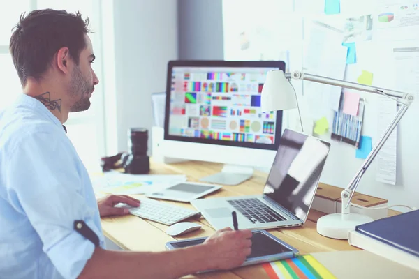 Porträt eines jungen Designers, der im Grafikstudio vor Laptop und Computer sitzt, während er online arbeitet. — Stockfoto