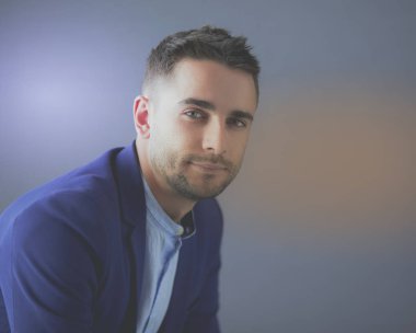 Gri arka planda yalnız oturan genç iş adamı.