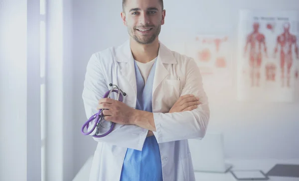 Jovem e confiante retrato médico masculino em pé no consultório médico. — Fotografia de Stock