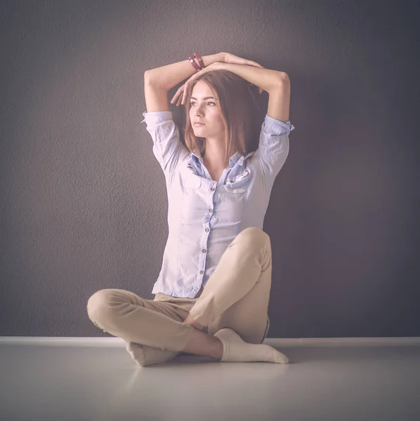 Portrait of a casual happy woman sitting on the floor on gray background — Stock Photo, Image