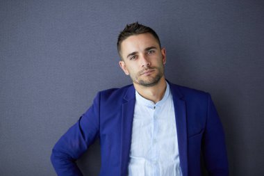 Gri arka planda yalnız oturan genç iş adamı.