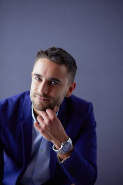 Gri arka planda yalnız oturan genç iş adamı.