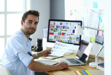 İnternette çalışırken bilgisayarın ve dizüstü bilgisayarın önünde grafik stüdyosunda oturan genç tasarımcının portresi.