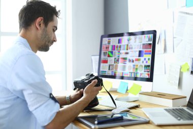 İnternette çalışırken bilgisayarın ve dizüstü bilgisayarın önünde grafik stüdyosunda oturan genç tasarımcının portresi.
