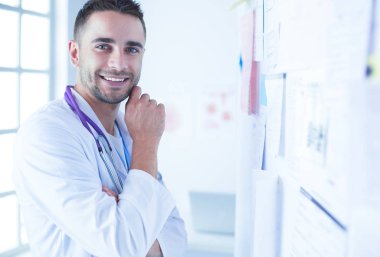 Genç ve kendinden emin erkek doktor portresi tıp ofisinde duruyor..