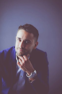 Gri arka planda yalnız oturan genç iş adamı.