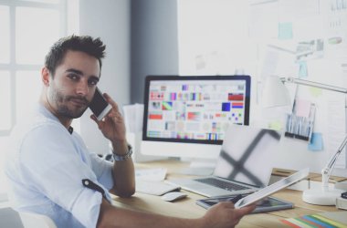 İnternette çalışırken bilgisayarın ve dizüstü bilgisayarın önünde grafik stüdyosunda oturan genç tasarımcının portresi