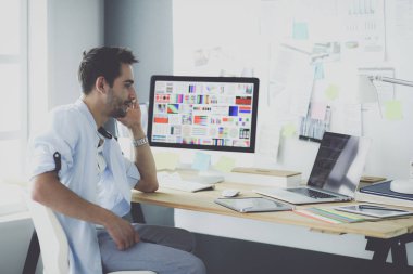 İnternette çalışırken bilgisayarın ve dizüstü bilgisayarın önünde grafik stüdyosunda oturan genç tasarımcının portresi.