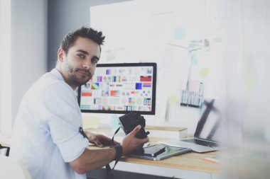 İnternette çalışırken bilgisayarın ve dizüstü bilgisayarın önünde grafik stüdyosunda oturan genç tasarımcının portresi.