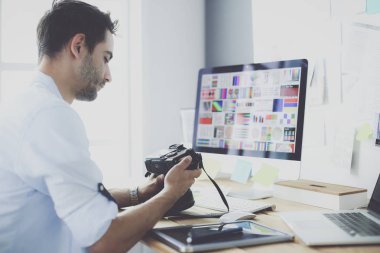 İnternette çalışırken bilgisayarın ve dizüstü bilgisayarın önünde grafik stüdyosunda oturan genç tasarımcının portresi.