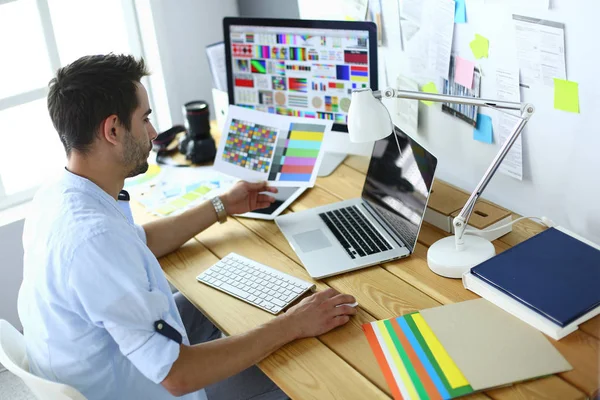 Porträt eines jungen Designers, der im Grafikstudio vor Laptop und Computer sitzt, während er online arbeitet. — Stockfoto