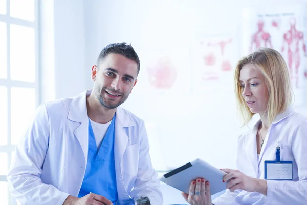 Schöner Arzt spricht mit junger Ärztin und macht sich Notizen, während er in seinem Büro sitzt. — Stockfoto