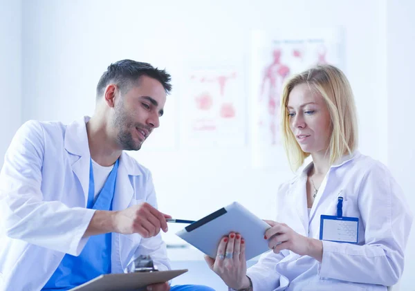 Snygg läkare pratar med ung kvinnlig läkare och antecknar när han sitter på sitt kontor. — Stockfoto