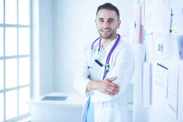 Jonge en zelfverzekerde mannelijke arts portret staan in medisch kantoor. — Stockfoto