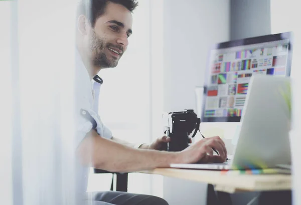 Retrato del joven diseñador sentado en el estudio gráfico frente a la computadora portátil y el ordenador mientras trabaja en línea. — Foto de Stock