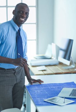 Ofiste bilgisayar ve planlarla çalışan Afrikalı Amerikalı bir mimar.