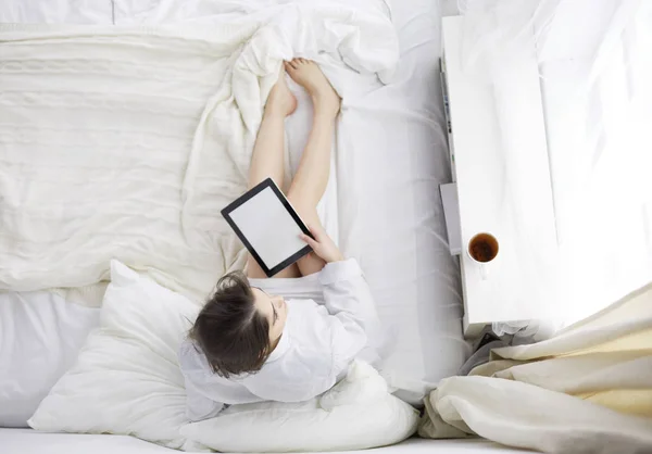 Porträtt av kvinna som använder tabletter och dricker kaffe när hon sitter på sängen på morgonen — Stockfoto